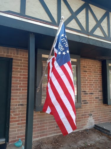 Reviewer's embroidered 1776 to 2026 Betsy Ross Flag flying from a flagpole attached to a brick house.