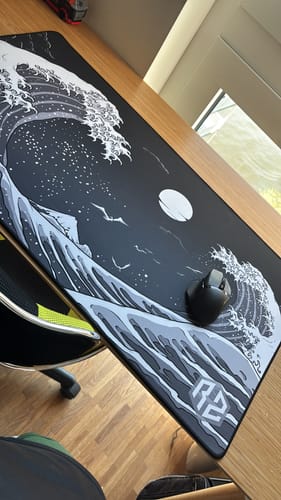 Rezensent zeigt das RZ Mousepad Kangawa Black mit einer Maus auf einem aufgeräumten Holztisch.