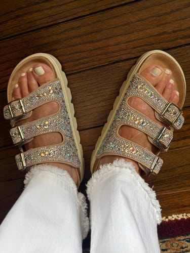 Customer wearing sparkly Corky's Rhinestone Threes Company Sandals, seen from a top-down angle on a wood floor.