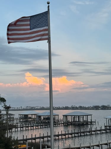 Customer's Ultra Heavy Duty American Flag waving on a flagpole with a cloudy sky over the water.