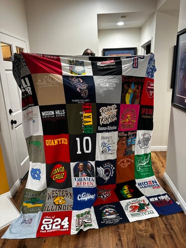 Customer holding up their large, colorful Project Repat T-Shirt Quilt, made from many t-shirts.
