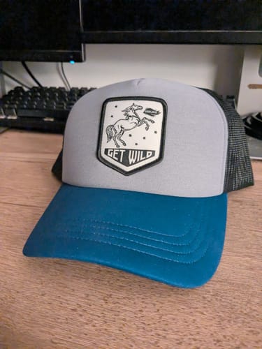 Customer's Big Foam Trucker Hat with a grey front, blue bill, and 'Get Wild' patch shown on a desk.