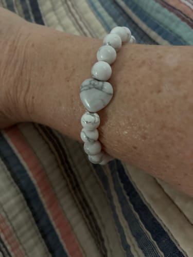 Reviewer wearing a white Howlite bracelet with marbled beads and a central heart-shaped stone on their wrist.