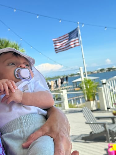 Reviewer holding a baby on a deck, with the Ultra Heavy Duty American Flag waving in the background over water.