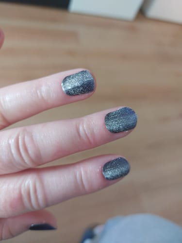 Kunde zeigt seine kurzen, schimmernden 'Midnight Cateye' UV-Gel-Nägel auf der Hand.