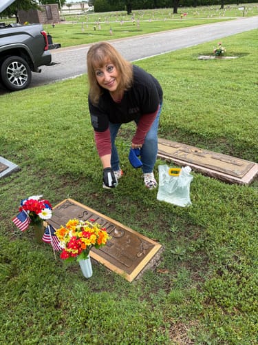 Reviewer wearing 'The Promise We Keep' tee while tending to a grave in a grassy cemetery.