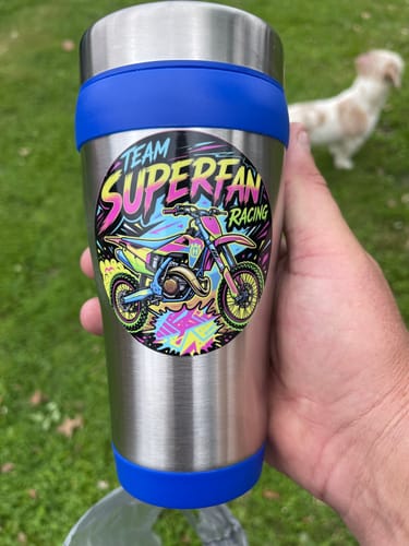 Customer holding a stainless steel travel mug with a colorful custom racing sticker on it outdoors.