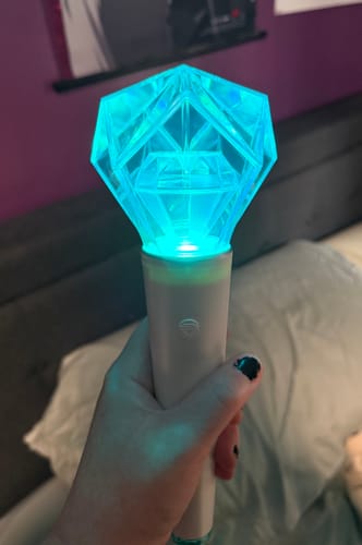 Reviewer holding the SHINEE OFFICIAL FANLIGHT, which is glowing with a bright aqua light.