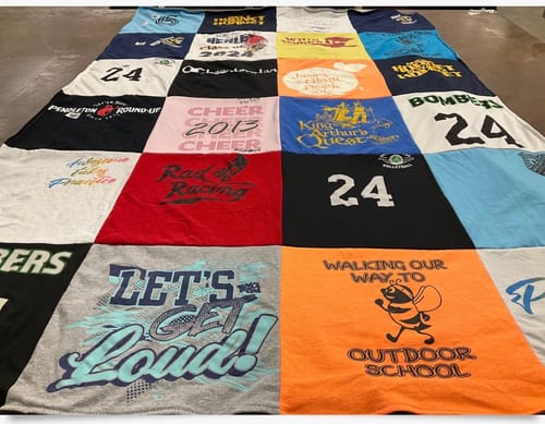 Customer's large Project Repat T-shirt Quilt, constructed from a grid of colorful, graphic t-shirts, laid out flat.