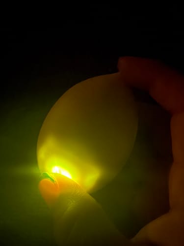 Reviewer holds the Lem Clitoral Massager, which glows with a bright yellow light in a dark setting.