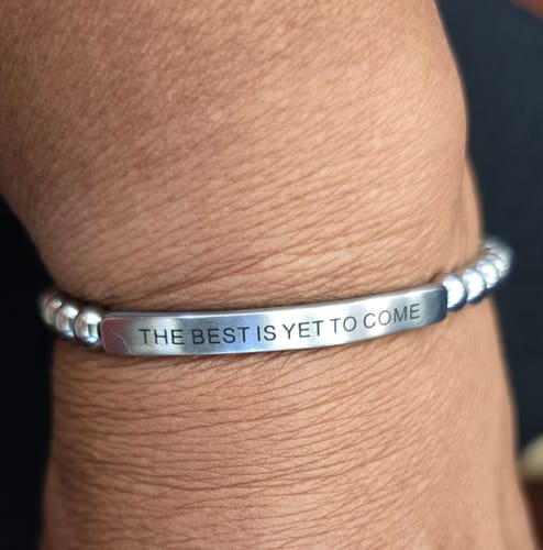 Reviewer's wrist with a silver beaded bracelet featuring the engraved message charm reading 'THE BEST IS YET TO COME'.