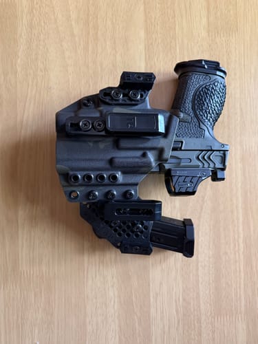 Customer's APX holster with a handgun and an attached magazine carrier laid on a wooden surface.