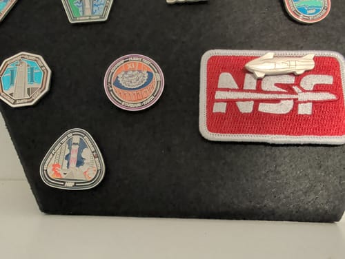 Customer's Starship Flight 12 pin displayed on a black board with other space-themed collector pins.