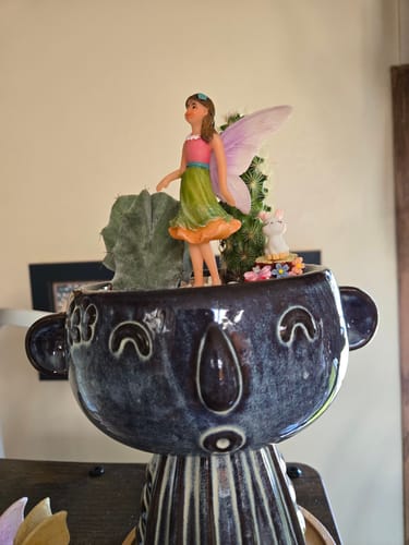 Reviewer's creative display with small cacti and figurines in a whimsical character pot.