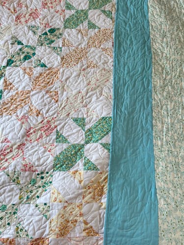 Customer's close-up of the finished Bloomcross quilt, showing the colorful top, teal binding, and a floral backing.
