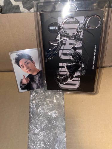 Customer's Xdinary Heroes keyring album in its packaging, displayed next to a photocard on a cardboard surface.