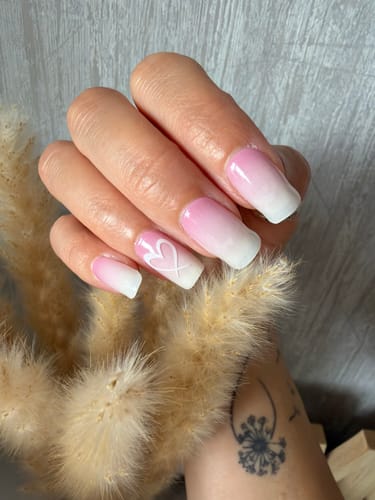 Hand einer Kundin mit den 'Babyboomer Pink' UV Gels, die einen rosa-weißen Ombré-Verlauf und einen Herz-Akzentnagel zeigen.