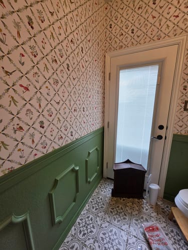 Customer's room showing the Kacie Wallpaper on the upper wall above green wainscoting and patterned floor tiles.