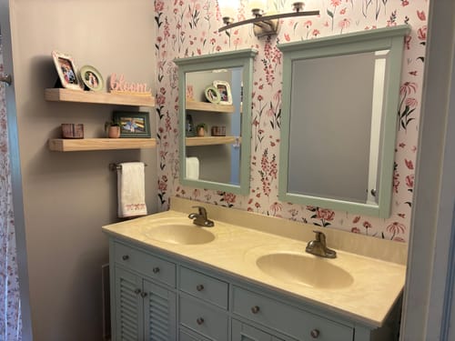 Customer's bathroom featuring Audrey Wallpaper with a pink floral pattern as an accent wall behind a double vanity.