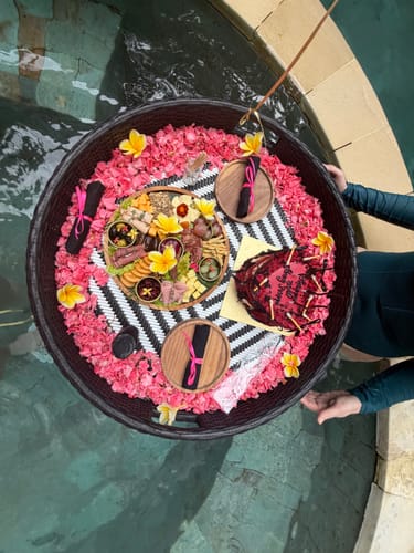 Customer's overhead view of a Luxury Charcuterie & Cheese Board and birthday cake on a decorated floating platter in a pool.