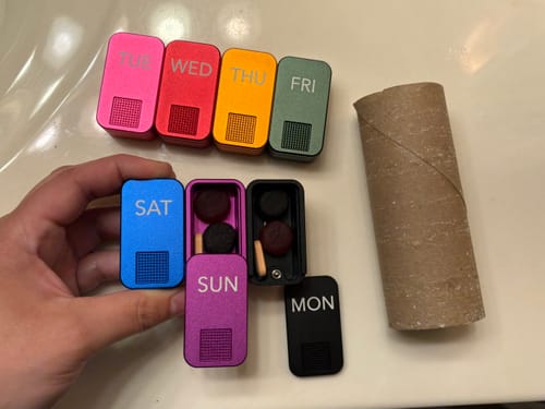 Customer shows the size of several colorful MagNano Case pill containers next to a toilet paper roll.