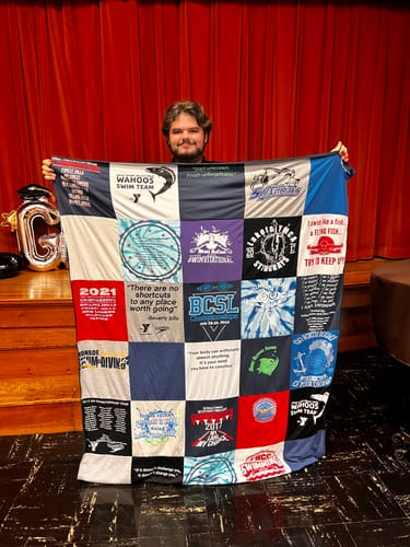 Customer holding a Project Repat T-Shirt Quilt, a graduation gift made from many swim team shirts.