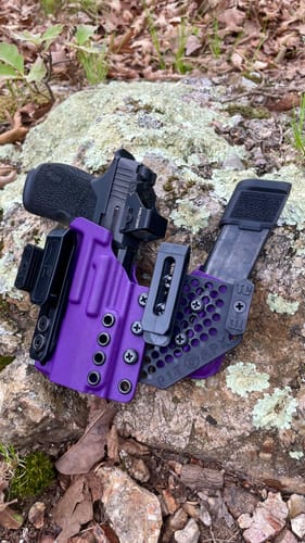 Customer's purple APX holster holding a handgun and attached magazine carrier, resting on a rock outdoors.