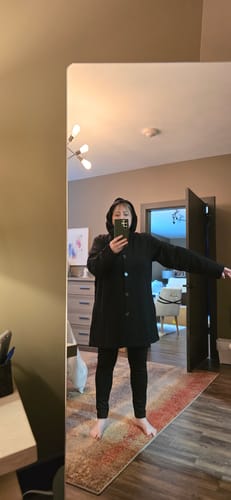 Reviewer in a mirror selfie wearing the black Edna Hooded Cardigan fully buttoned with the hood up.