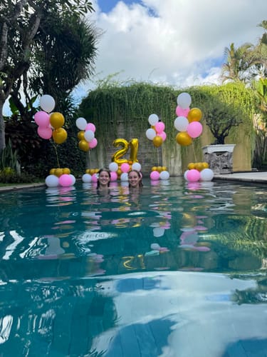 Customer's pink and gold Balloon Centerpiece arrangements in a pool for a 21st birthday, with two people smiling.