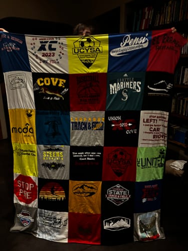 Customer holding up their large Project Repat T-Shirt Quilt, made from a colorful collage of t-shirts.