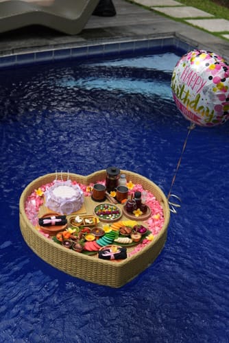 Customer's Birthday Surprise Package on a heart-shaped floating tray with a cake and balloon in a pool.