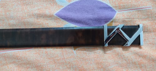 Customer's close-up of the Bacca Bucci leather belt laid on a patterned surface, showing the dark strap and stylized silver buckle.
