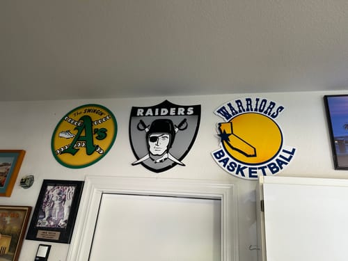 Customer's Las Vegas Raiders vintage shield metal art mounted on a white wall between two other sports logos.