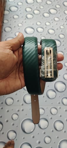 A reviewer's hand holding the coiled green Bacca Bucci belt, showing its textured strap and wrapped buckle.