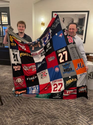 Reviewer and another person holding up a large Project Repat T-Shirt Quilt made from colorful jerseys.