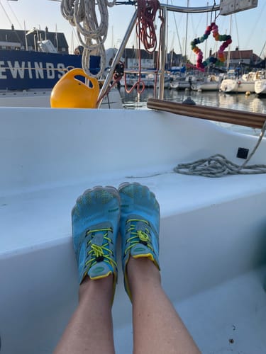 Customer wearing blue Free Ⅰ - Barefoot Shoes with their feet propped up on a boat in a harbor.