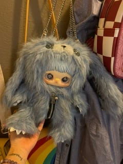 Customer holding the fluffy blue MayMei Rebel Doll Backpack, which has large eyes and a chain strap.