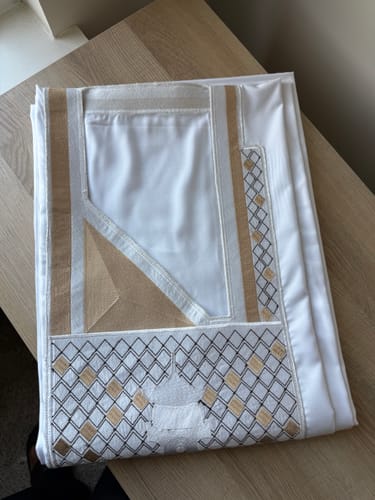 Customer's folded White Concord Agbada on a wooden table, showing detailed gold and black embroidery.