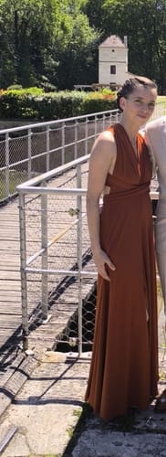 Cliente portant la longue robe CECILIA terracotta avec un décolleté croisé sur un pont en extérieur.