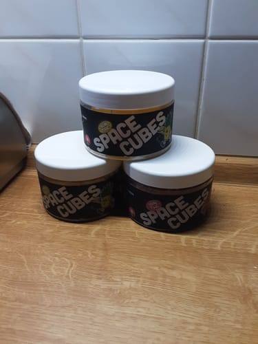 Rezensent zeigt drei Behälter der THC Space Cubes, die auf einem Holztisch gestapelt sind.