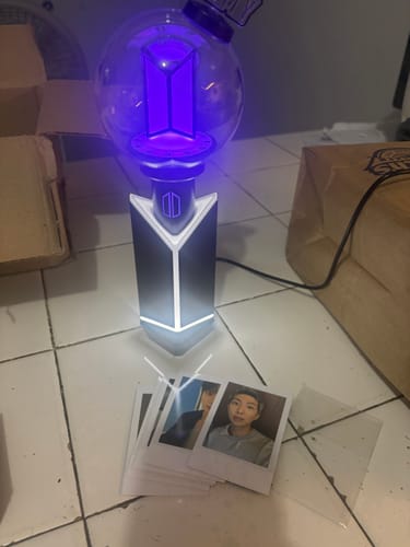 Customer's BTS Official Light Stick Ver.4 glowing purple, standing on a floor with photo cards arranged in front.