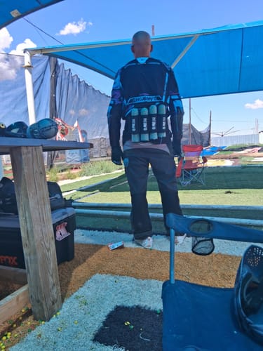 Customer wearing the PRO DNA™ SPRINT PACK, seen from behind, loaded with nine pods at a paintball field.