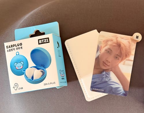 Customer's photo of a BTS RM photocard in a sleeve next to a box of BT21 earplugs.