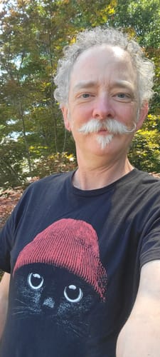 Reviewer standing outdoors wearing the black Statement Made t-shirt with a graphic of a cat in a red beanie.