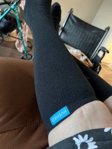 Reviewer wearing black Performance Eucalyptus Compression Socks while resting, with a walker and wheelchair in the background.