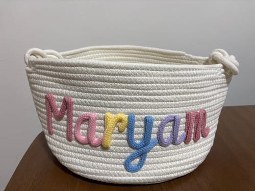 Customer's personalized white knitted basket with the name 'Maryam' in multicolor yarn.