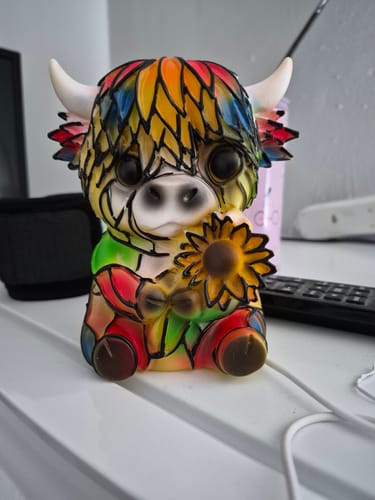 Customer's colorful Highland Cow LED Night Light on a table. The figurine has a stained-glass design and is holding a sunflower.