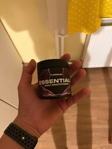 A reviewer holding the black Essentials Multivitamin container in their open palm.