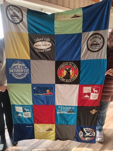Customer holding up a large, colorful Project Repat T-Shirt Quilt made with various community t-shirts from Herron Island.