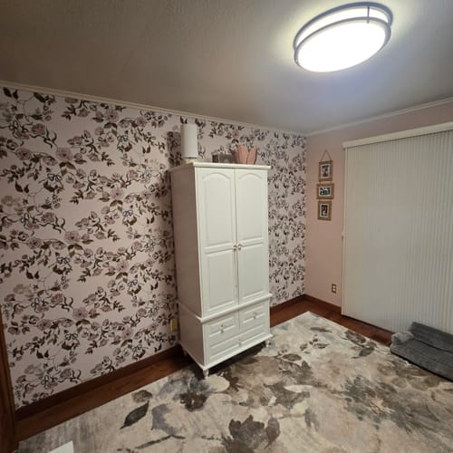 Customer's room showing the floral Lettie Wallpaper on an accent wall behind a white wardrobe.
